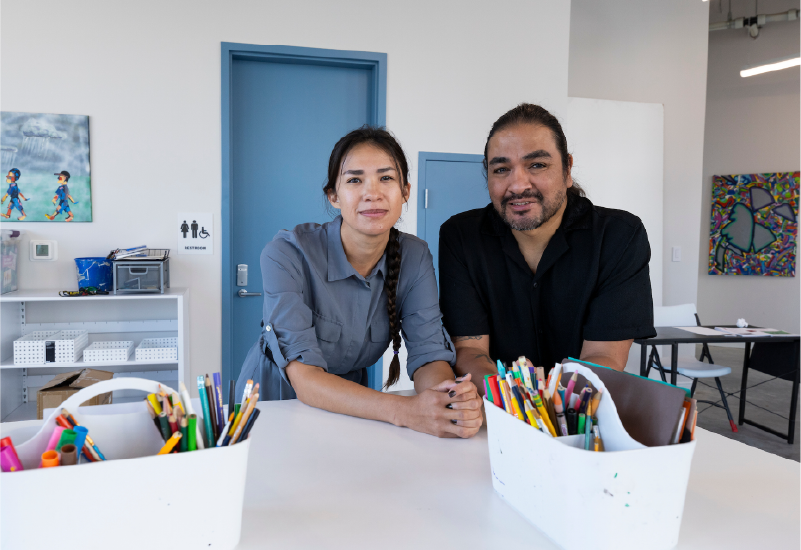 Two people in a room with crafts on the surface in front of them.